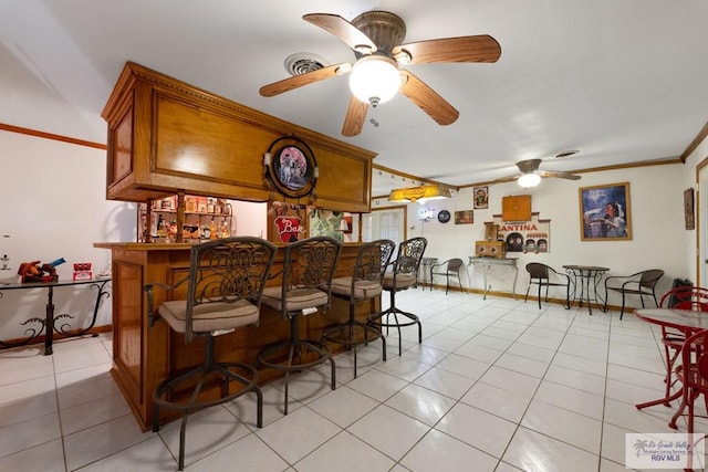 bar with light tile patterned floors, visible vents, a bar, ornamental molding, and a ceiling fan
