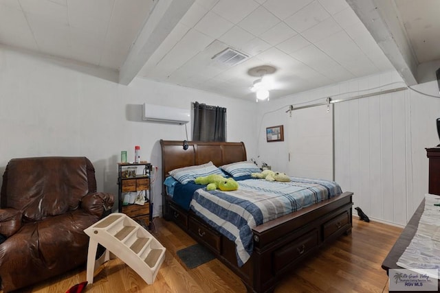 bedroom with visible vents, wood finished floors, beamed ceiling, and a wall unit AC