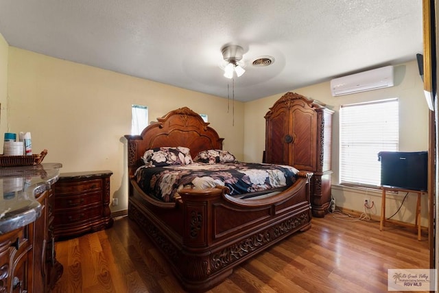 bedroom featuring ceiling fan, visible vents, baseboards, wood finished floors, and a wall mounted air conditioner