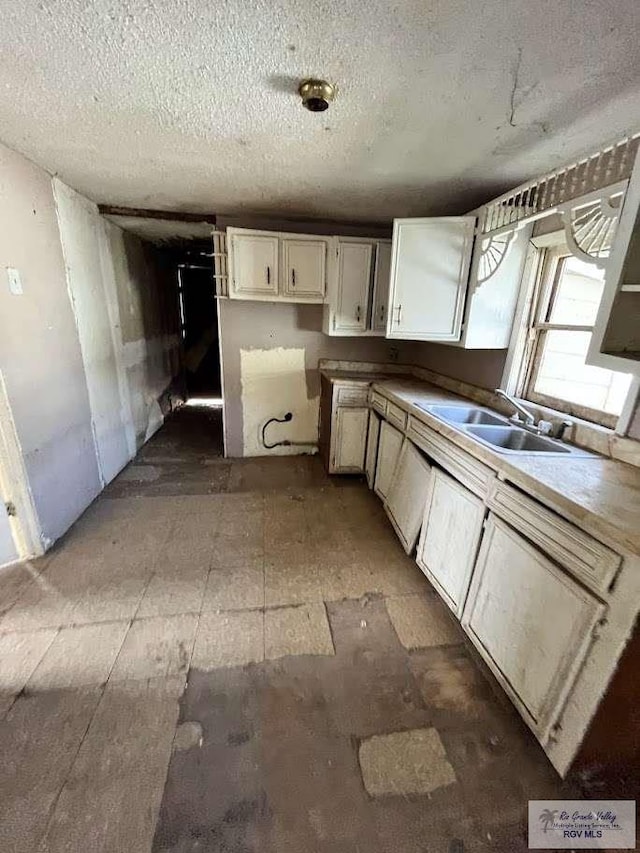 kitchen with a textured ceiling, white cabinets, and sink