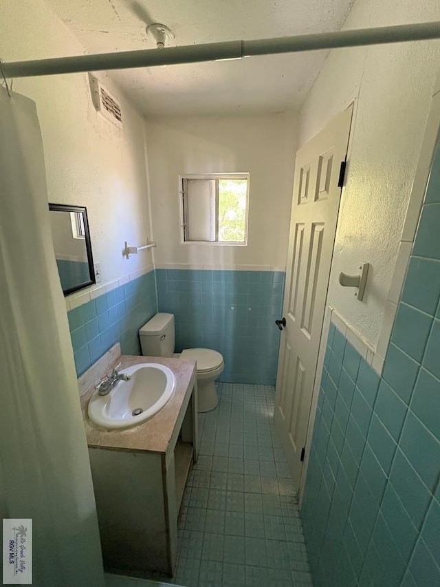 half bathroom featuring vanity, tile patterned flooring, a wainscoted wall, toilet, and tile walls