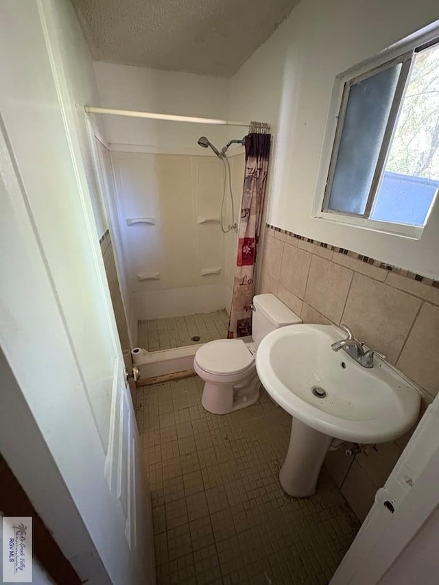 bathroom featuring a shower stall, toilet, a sink, wainscoting, and tile walls