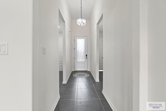 doorway to outside with dark tile patterned floors and a notable chandelier