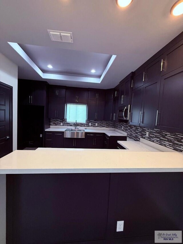 7377 San Andres St, Brownsville, TX 78520 - kitchen with stainless steel microwave, a raised ceiling, tasteful backsplash, light countertops, and a sink