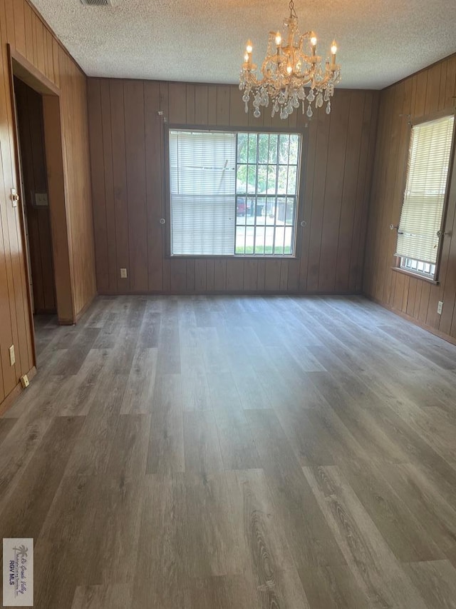 unfurnished room with hardwood / wood-style flooring, a notable chandelier, a textured ceiling, and wooden walls