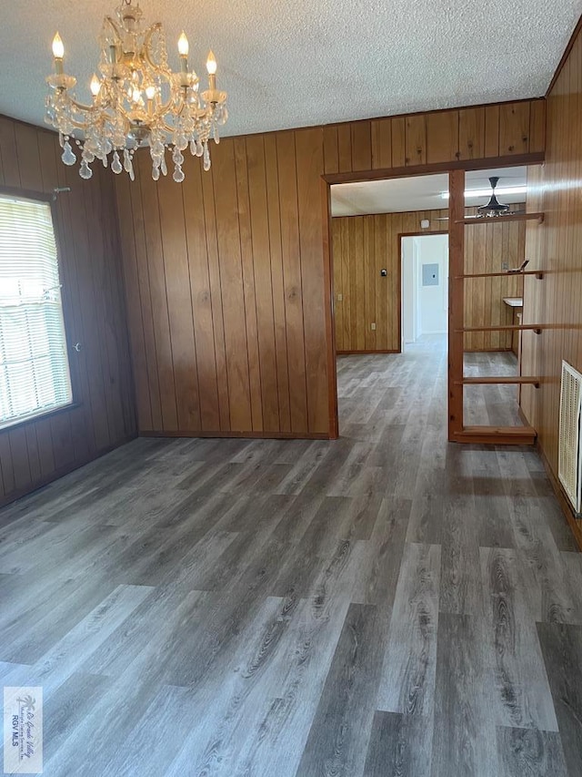 unfurnished dining area featuring a textured ceiling, ceiling fan with notable chandelier, wood walls, and dark wood-type flooring