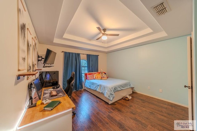 bedroom featuring a raised ceiling, a ceiling fan, baseboards, wood finished floors, and visible vents