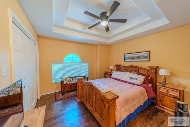 bedroom with ceiling fan, wood finished floors, a raised ceiling, baseboards, and a closet