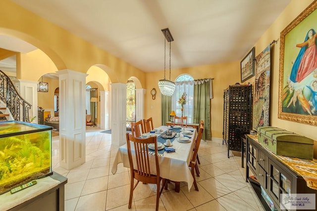 dining room with ornate columns, arched walkways, light tile patterned floors, and stairway