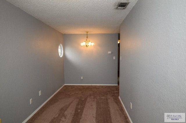 carpeted empty room featuring visible vents, baseboards, an inviting chandelier, a textured ceiling, and a textured wall