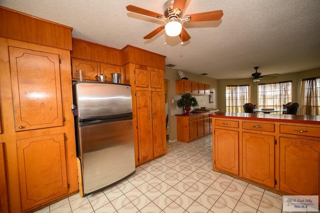 kitchen with a textured ceiling, brown cabinets, dark countertops, and freestanding refrigerator