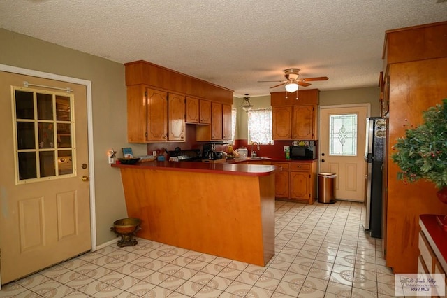 kitchen featuring brown cabinets, a ceiling fan, freestanding refrigerator, a peninsula, and black microwave