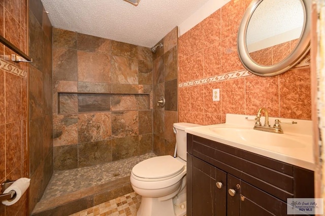 bathroom featuring toilet, a textured ceiling, a tile shower, tile walls, and vanity