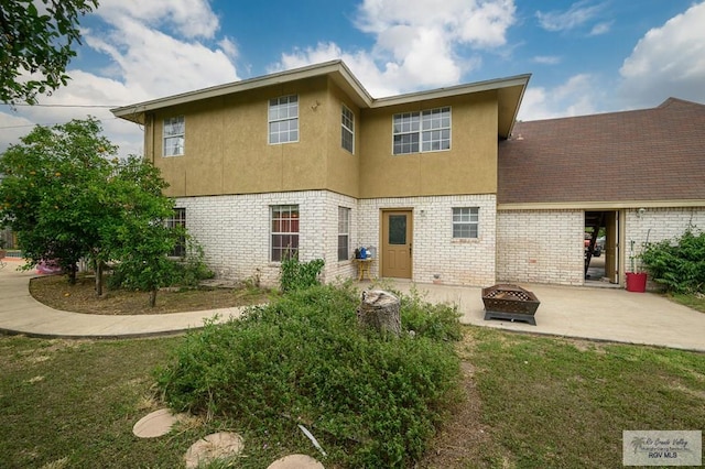 rear view of property with brick siding, an outdoor fire pit, stucco siding, a lawn, and a patio