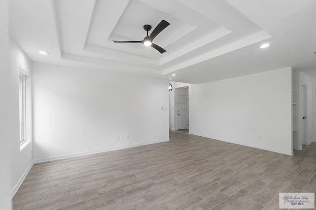 empty room featuring ceiling fan, light hardwood / wood-style floors, and a tray ceiling