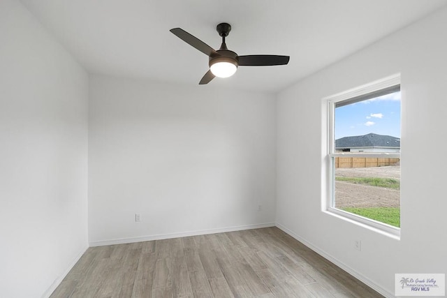 empty room featuring a mountain view, light hardwood / wood-style flooring, and ceiling fan