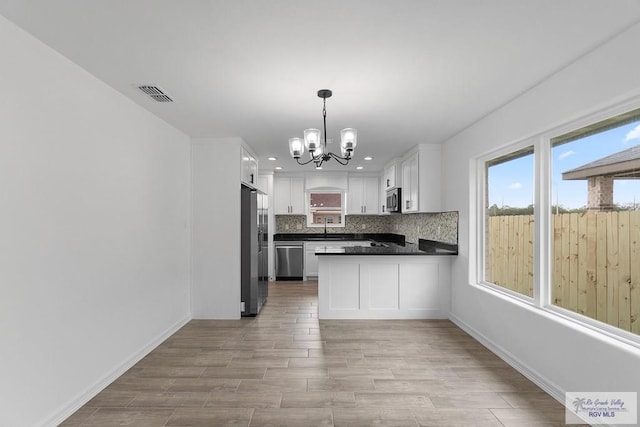 kitchen with a chandelier, backsplash, white cabinetry, and stainless steel appliances