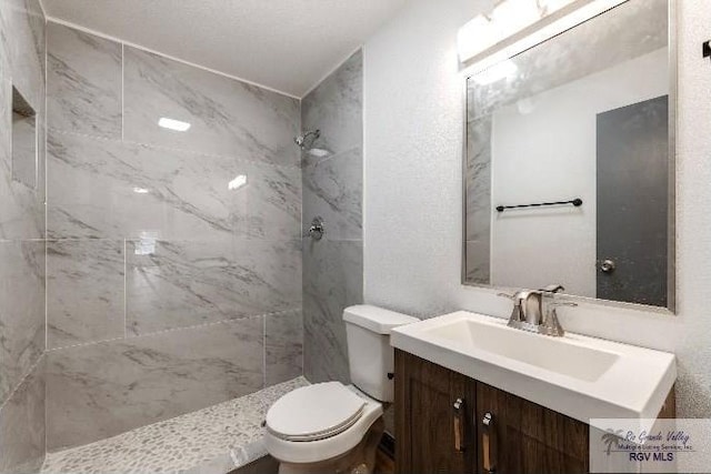 bathroom with toilet, tiled shower, and vanity