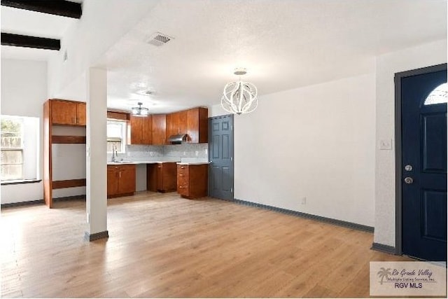 kitchen featuring a notable chandelier, baseboards, light countertops, brown cabinetry, and light wood finished floors