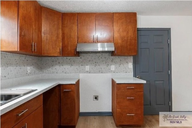kitchen featuring under cabinet range hood, light wood finished floors, light countertops, and brown cabinetry