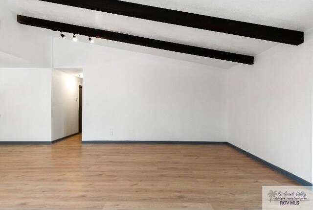 spare room with light wood finished floors, lofted ceiling with beams, and baseboards