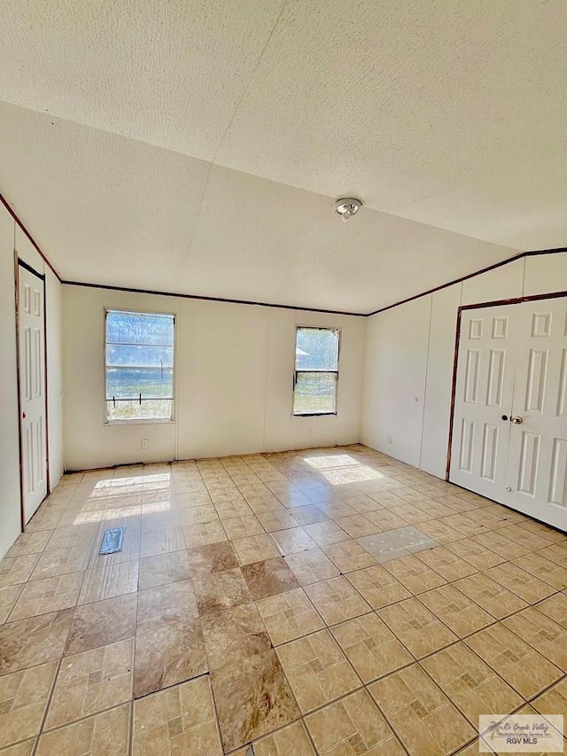 unfurnished bedroom featuring lofted ceiling, ornamental molding, and a textured ceiling