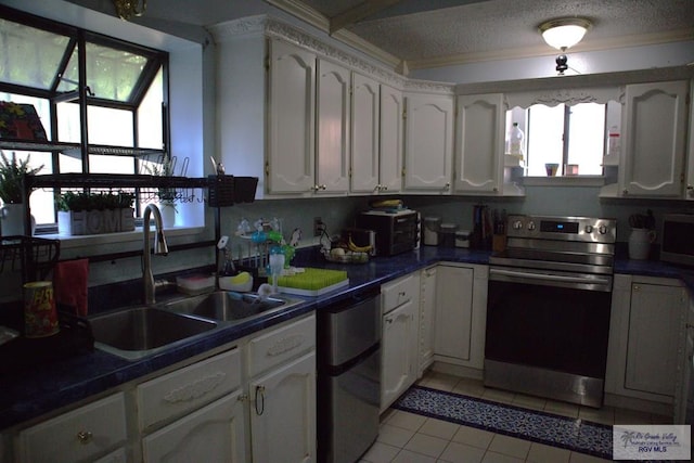 kitchen with appliances with stainless steel finishes, a textured ceiling, sink, light tile patterned floors, and white cabinetry