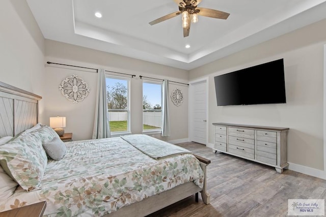 bedroom with baseboards, a raised ceiling, wood finished floors, and recessed lighting