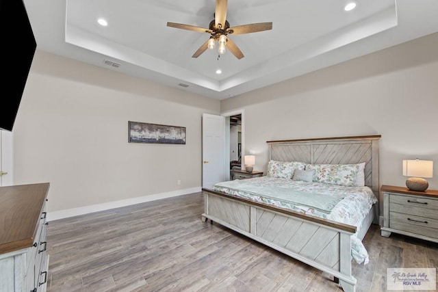 bedroom with wood finished floors, a raised ceiling, visible vents, and baseboards