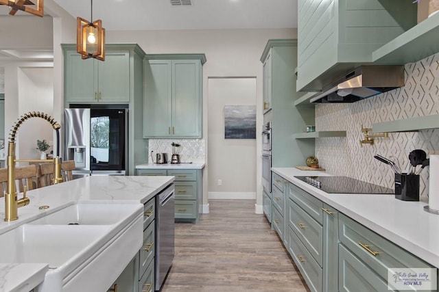 kitchen featuring green cabinetry, a sink, appliances with stainless steel finishes, wall chimney exhaust hood, and pendant lighting