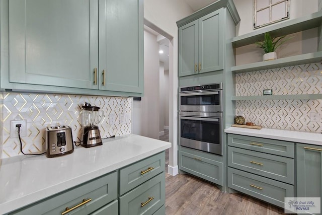 kitchen featuring stainless steel double oven, light countertops, decorative backsplash, open shelves, and green cabinetry