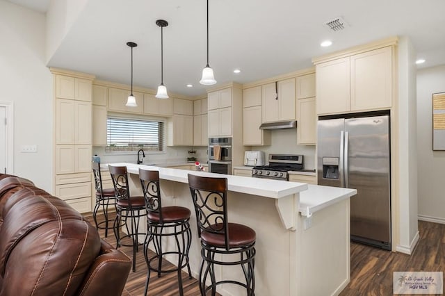 kitchen with a kitchen bar, a center island, appliances with stainless steel finishes, pendant lighting, and cream cabinets