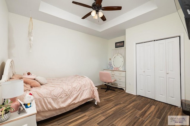 bedroom with dark wood-type flooring, ceiling fan, a raised ceiling, and a closet