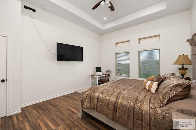 bedroom with ceiling fan, a tray ceiling, and dark hardwood / wood-style flooring