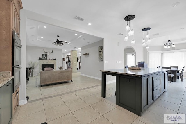 kitchen featuring a center island, dark stone counters, decorative light fixtures, a tray ceiling, and ceiling fan with notable chandelier