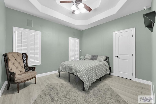 bedroom with a tray ceiling, ceiling fan, and light wood-type flooring