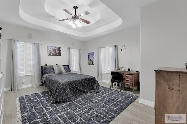 bedroom with hardwood / wood-style floors, ceiling fan, and a raised ceiling