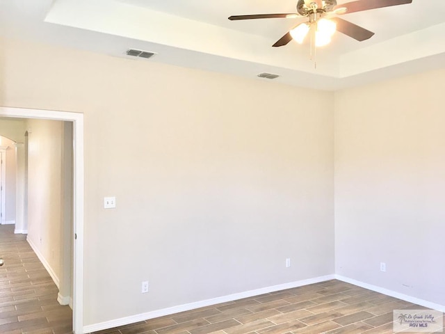 empty room featuring a tray ceiling, ceiling fan, and hardwood / wood-style floors