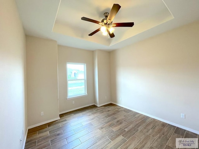 empty room with a tray ceiling, ceiling fan, and wood-type flooring