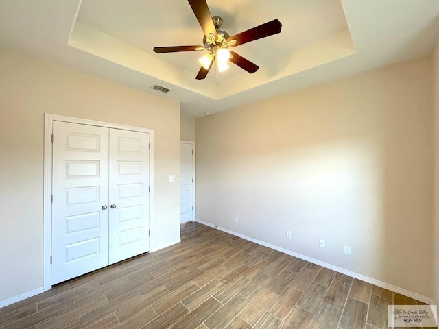 unfurnished bedroom featuring ceiling fan, a raised ceiling, wood-type flooring, and a closet