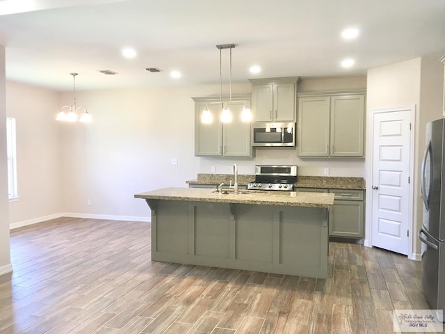 kitchen featuring a kitchen island with sink, hardwood / wood-style floors, hanging light fixtures, and appliances with stainless steel finishes