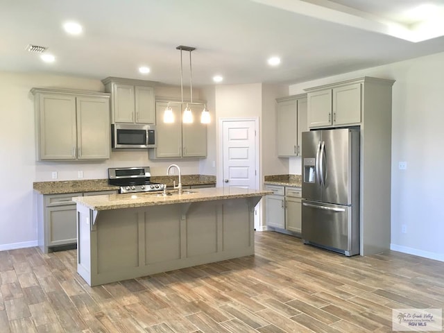 kitchen featuring a center island with sink, sink, hanging light fixtures, light hardwood / wood-style floors, and stainless steel appliances