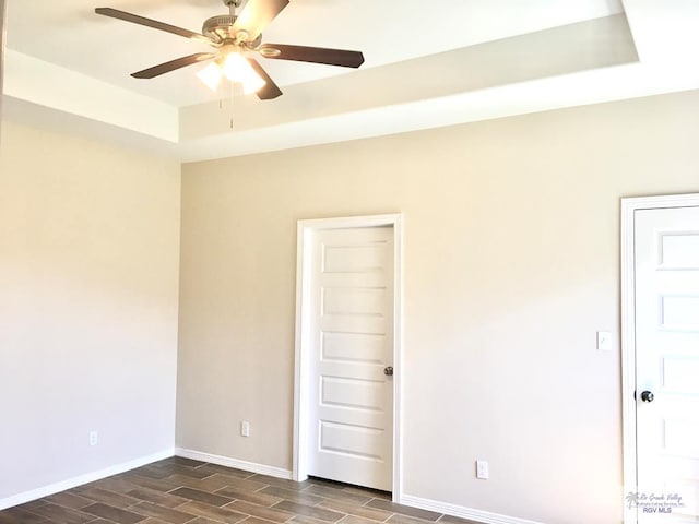 unfurnished room featuring a tray ceiling, ceiling fan, and dark wood-type flooring