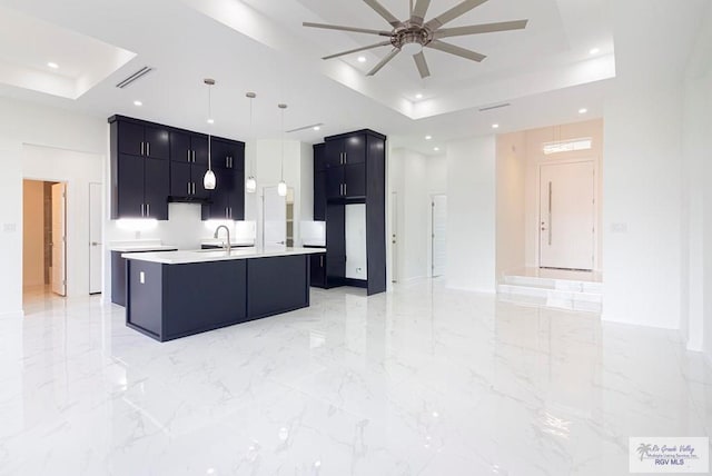 kitchen with pendant lighting, a center island with sink, a raised ceiling, and ceiling fan