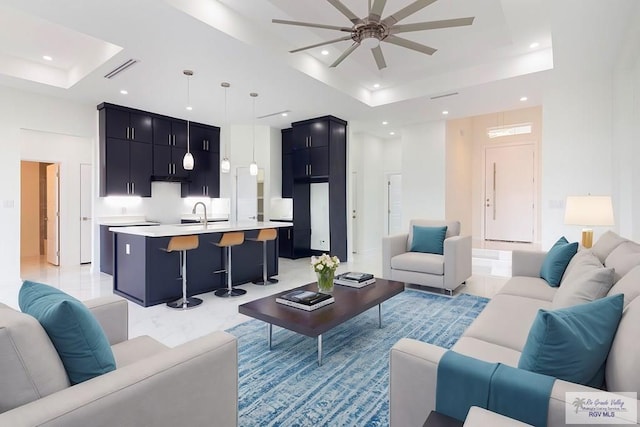 living room with a raised ceiling, ceiling fan, and sink