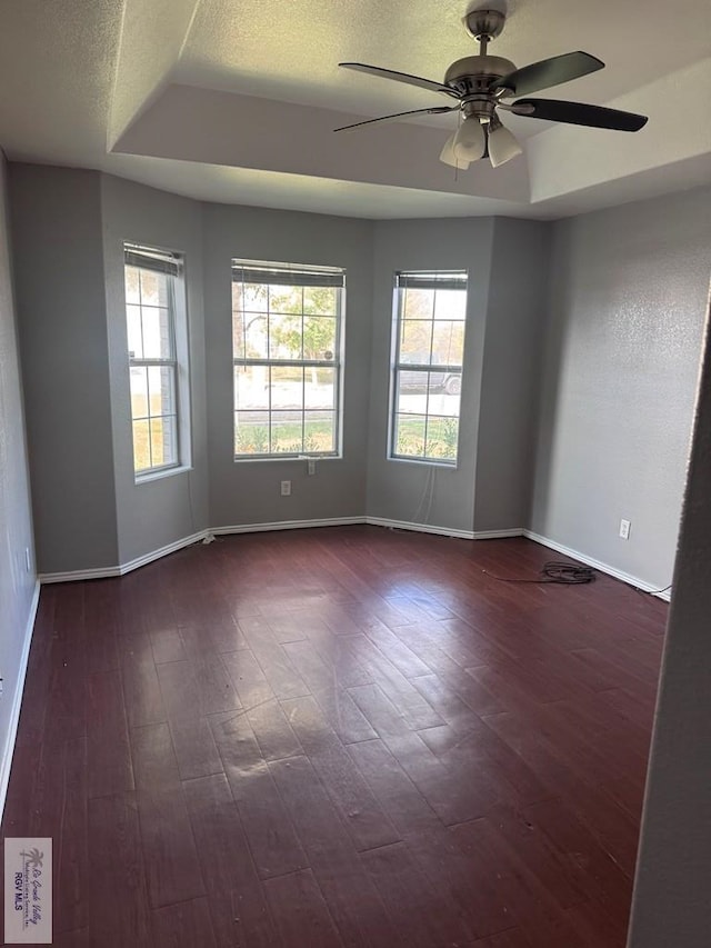 unfurnished room featuring dark hardwood / wood-style floors, ceiling fan, and a tray ceiling