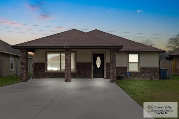 view of front facade featuring driveway, a shingled roof, a front yard, and stucco siding