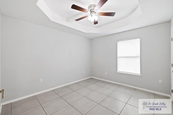 tiled spare room with baseboards, a tray ceiling, and a ceiling fan