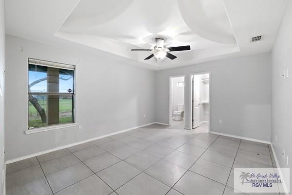 tiled empty room with a ceiling fan, a tray ceiling, visible vents, and baseboards