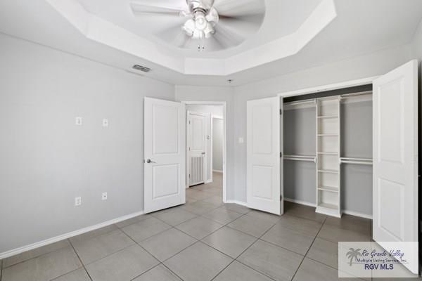 unfurnished bedroom with tile patterned flooring, visible vents, baseboards, a closet, and a tray ceiling